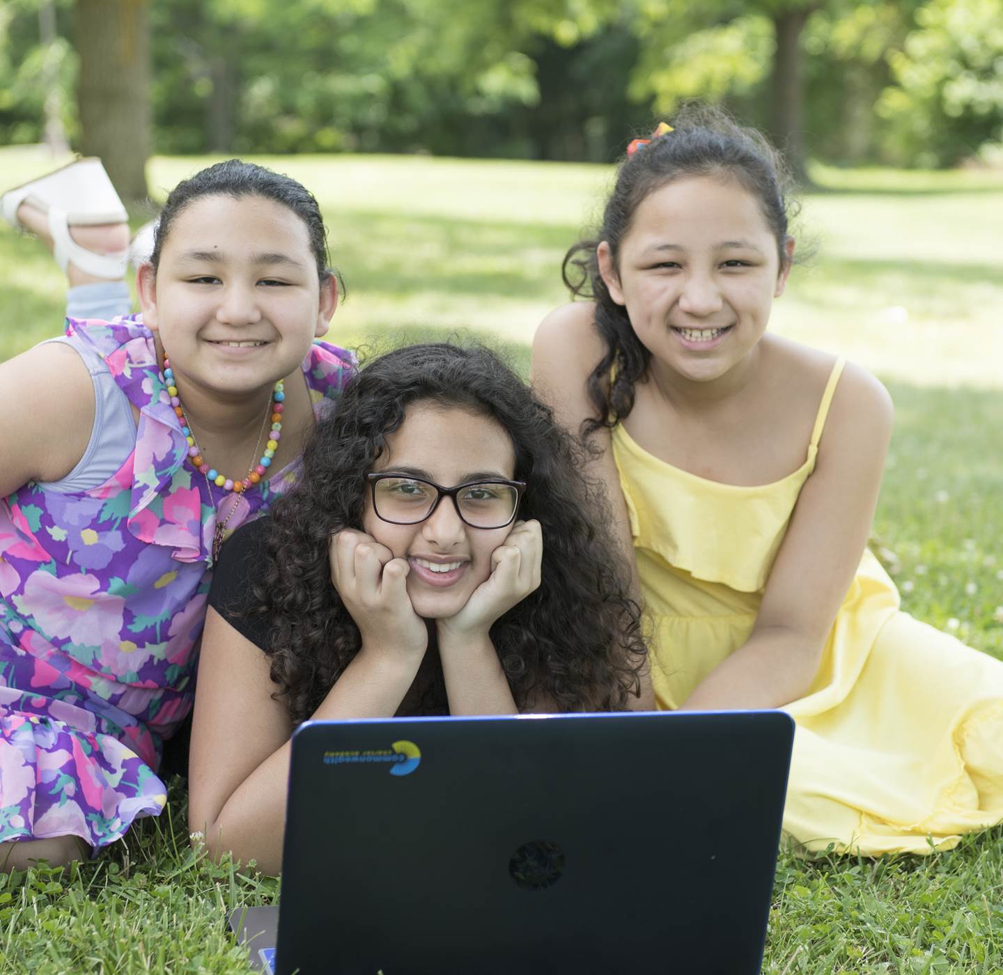 Three girls smiling behind a laptop.