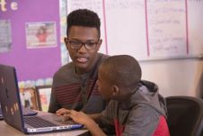 Two students talking in front of a laptop.