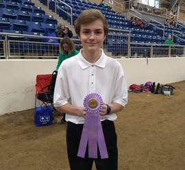 A boy at the farm show holding up a ribbon.