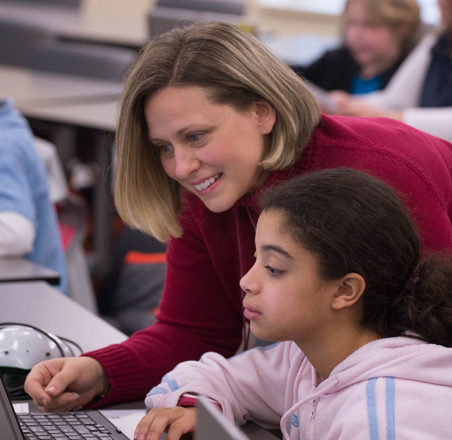 A teacher helping a student on a laptop.