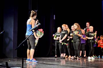 A woman handing out flowers to girls on stage.