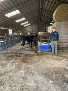 CCA graduate Brandon standing a barn with his cow.